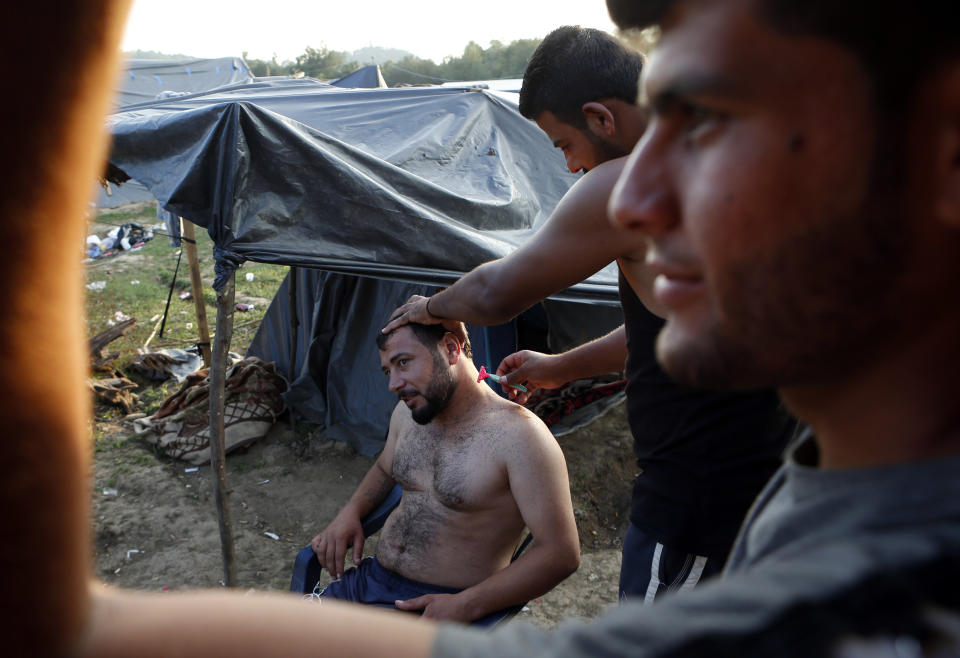 In this photo taken on Tuesday, Aug. 14, 2018, a migrant man receives a haircut in a makeshift migrant camp in Velika Kladusa, 500 kms northwest of Sarajevo, Bosnia. Impoverished Bosnia must race against time to secure proper shelters for at least 4,000 migrants and refugees expected to be stranded in its territory during coming winter. The migrant trail shifted toward Bosnia as other migration routes to Western Europe from the Balkans were closed off over the past year. (AP Photo/Amel Emric)