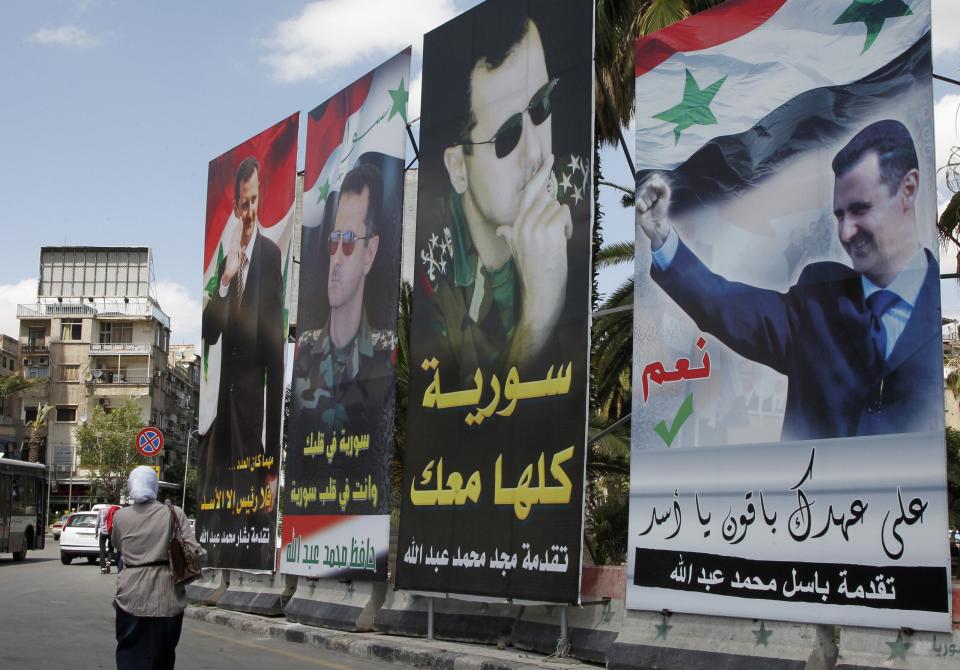 A woman walks past election posters of Syria's President Bashar al-Assad along a street in Damascus June 2, 2014. (REUTERS/Khaled al-Hariri)