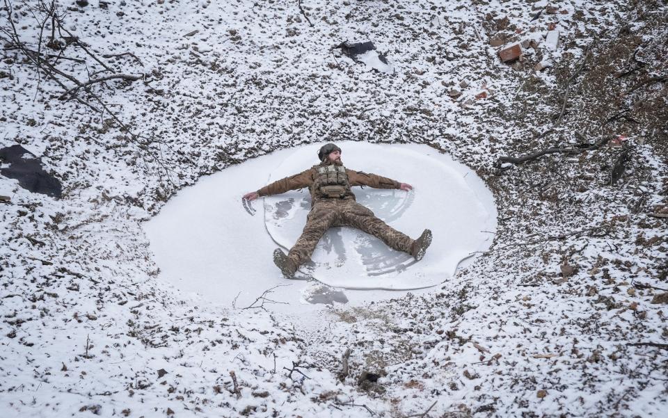 Soldier makes a snow angel in a bomb crater