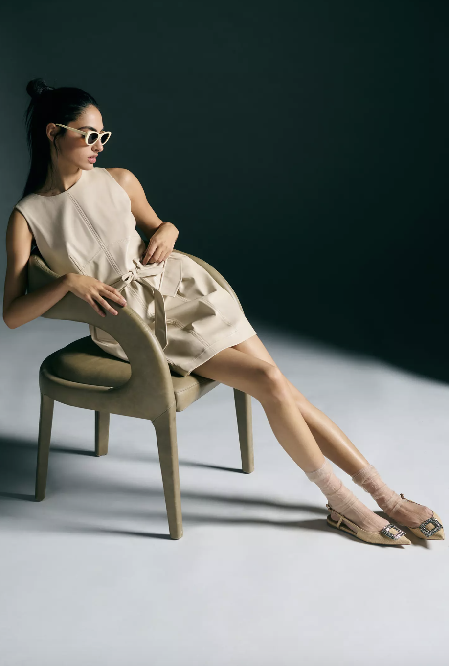 model sitting in chair wearing light beige belted Shoshanna Faux Leather Dress (photo via Anthropologie)