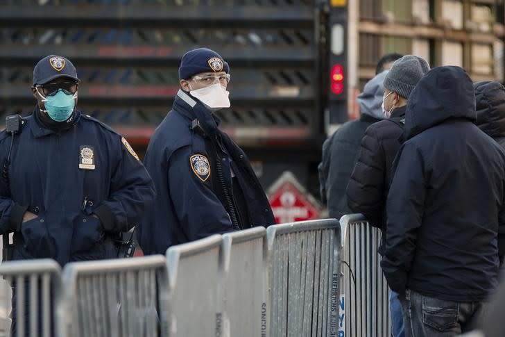 Policías de la ciudad de Nueva York utilizan máscarillas mientras observan a personas que hacen fila para realizarse pruebas por coronavirus fuera del Hospital Center, en el vecindario de Queens, Nueva York