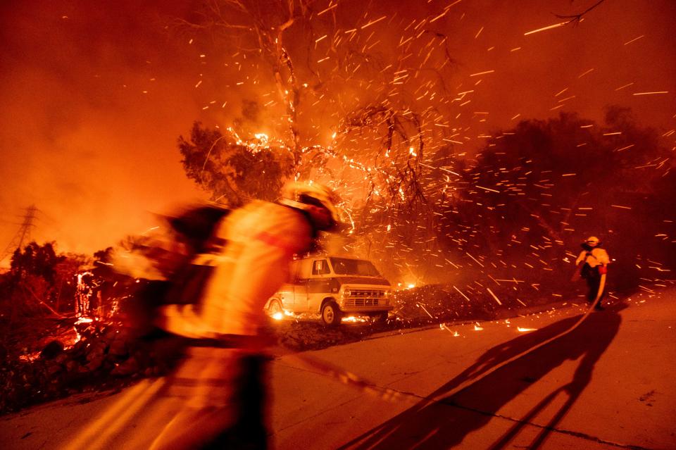 Firefighters battling the Bond Fire haul a hose while working to save a home in the Silverado community in Orange County, Calif., on Thursday, Dec. 3, 2020. 