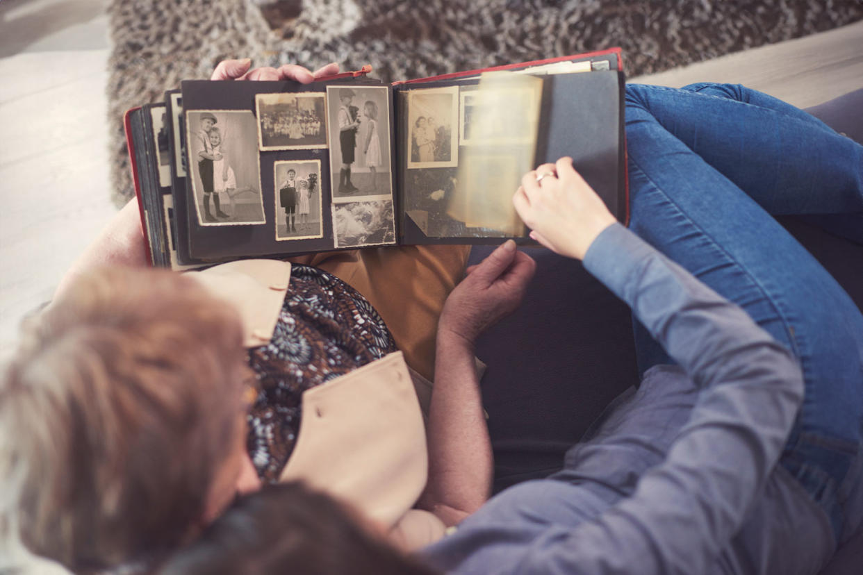 Young woman on sofa with grandmother looking at photo album Getty Images/Gpointstudio