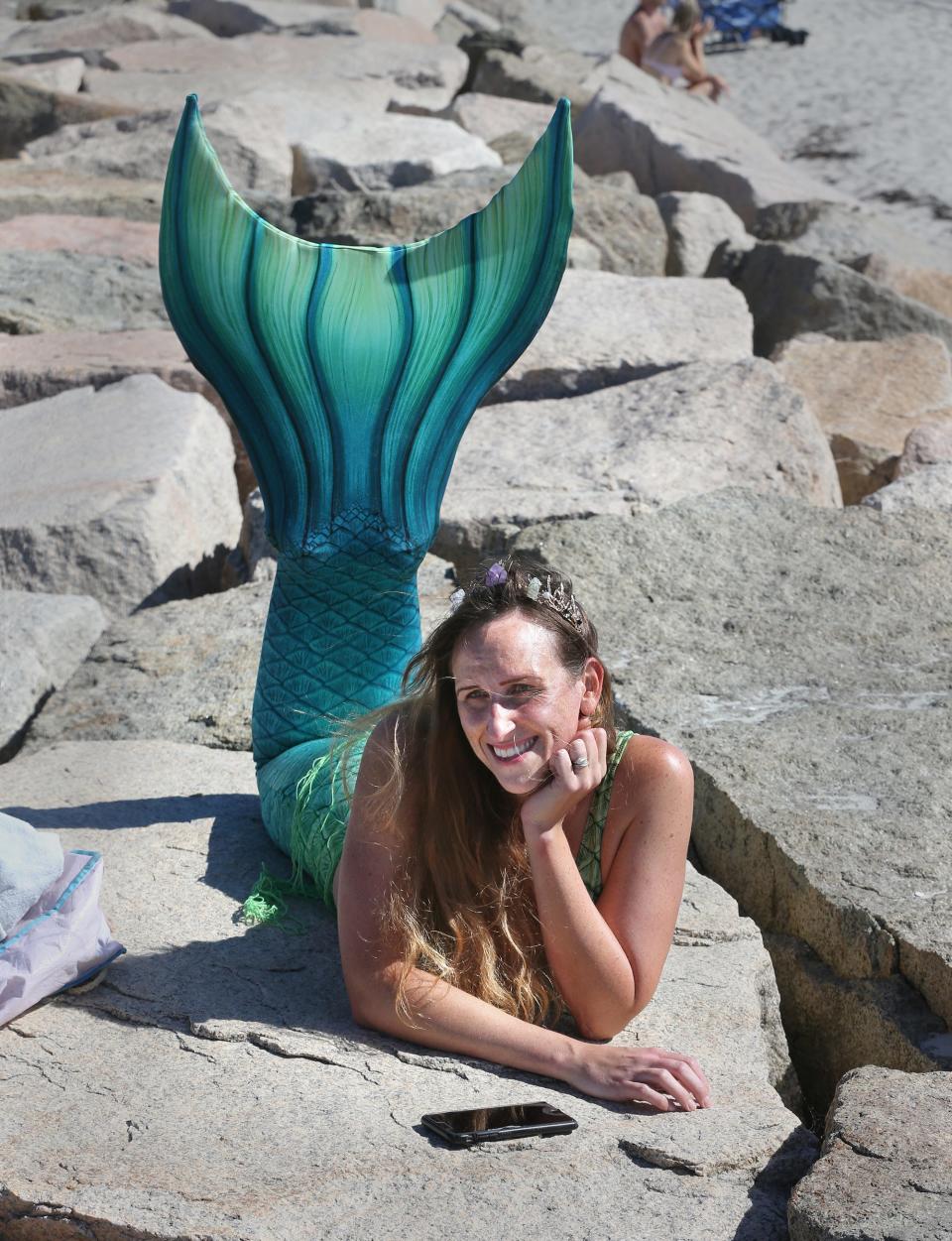 Mermaid Lavinia lies on the jetty rocks while a reporter interviews her at Wells Beach Aug. 23, 2023.