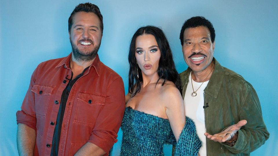 Luke Bryan in an orange shirt smiles next to Katy Perry in a turquoise patterned shirt and Lionel Richie in a green jacket