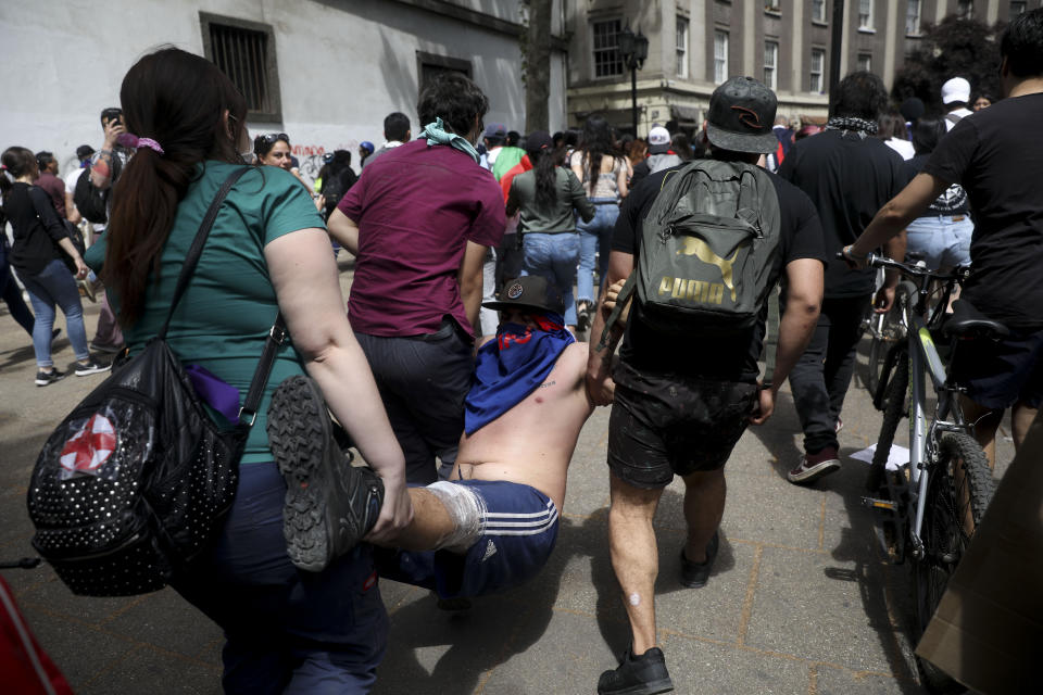 Demonstrators carry a wounded man during clashes with police in Santiago, Chile, Wednesday, Oct. 23, 2019. Rioting, arson attacks and violent clashes wracked Chile as the government raised the death toll in an upheaval that has almost paralyzed the South American country long seen as the region's oasis of stability. (AP Photo/Rodrigo Abd)