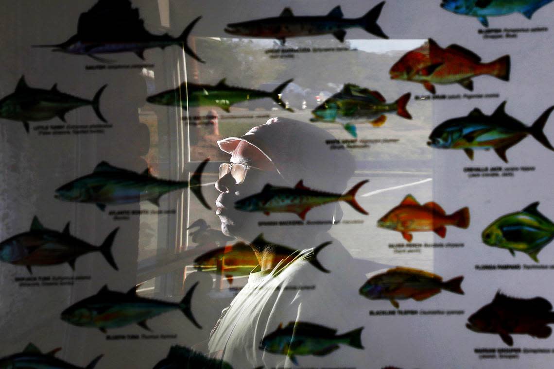 Ricky Moore, chef and owner of Saltbox Seafood Joint, is reflected in a poster of North Carolina fish in the dining area of the restaurant on Monday, Nov. 14, 2022, in Durham, N.C. Moore is The News & Observer’s 2022 Tar Heel of the Year.