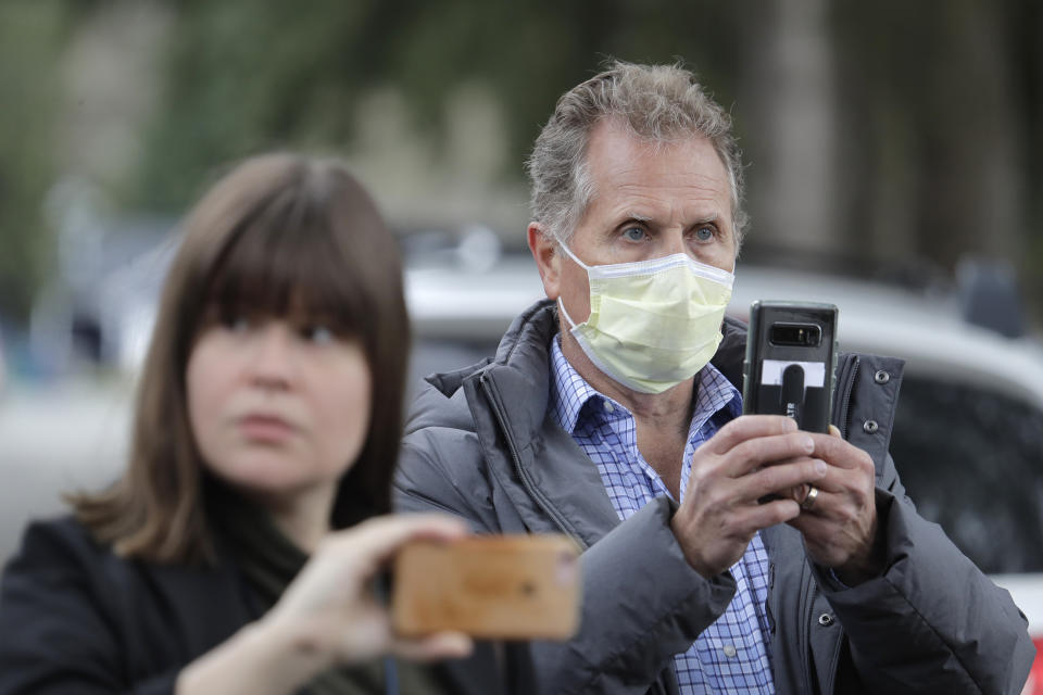 In this March 11, 2020, photo, Scott Sedlacek, right, who has tested positive for the COVID-19 coronavirus, wears a mask as he stands near reporters and listens to a spokesman for Life Care Center in Kirkland, Wash., during a daily press briefing. Sedlacek's father, Chuck, who also has tested positive, lives in the facility, which has been at the center of the COVID-19 coronavirus outbreak in the state, and Sedlacek said he and his siblings have barely spoken to their father, who has blindness and neuropathy, and difficulty using a phone, saying he is more of an "inmate" than a patient. Residents of assisted living facilities and their loved ones are facing a grim situation as the coronavirus spreads across the country, placing elderly people especially at risk. (AP Photo/Ted S. Warren)