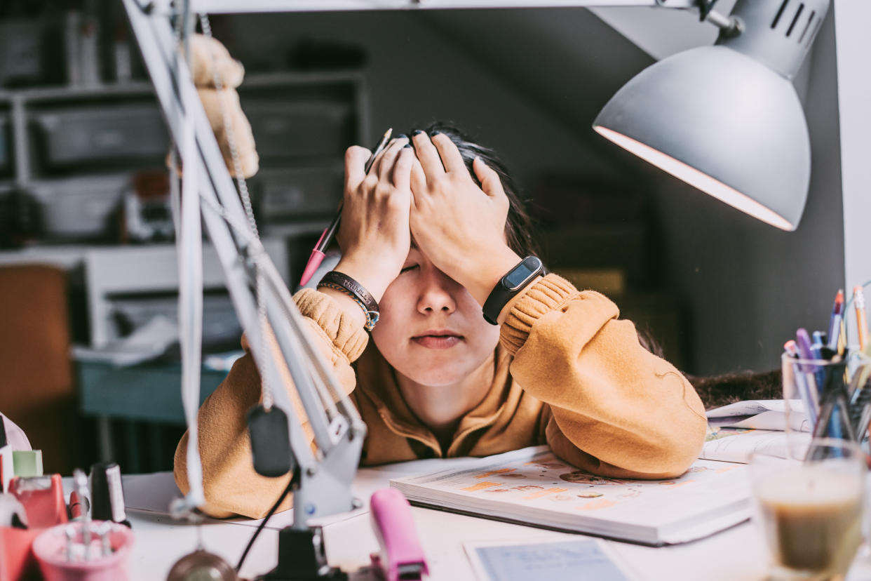 Stressed student sitting at desk with hands covering forehead