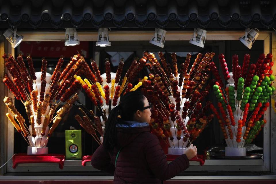 In this Thursday, Dec. 29, 2016 photo, a woman buys a sugar-coated haws on a stick at a street vendor in Beijing. Sugar-coated haws, also known as "Tanghulu," is a traditional Chinese candied snack popular in northern China, especially in Beijing during the winter season. (AP Photo/Andy Wong, File)