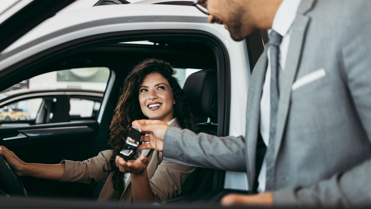 Happy and beautiful middle age business woman buying new car at showroom.