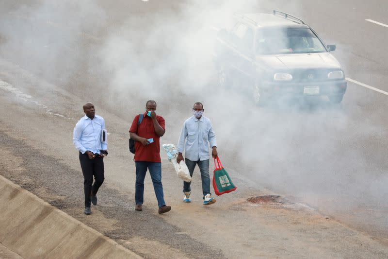 People wearing protective face masks walk through smoke, as authorities ease the lockdown following the coronavirus disease (COVID-19) outbreak in Abuja