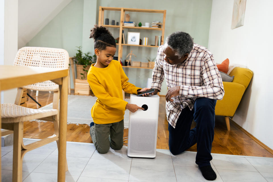 A young boy showing to his grandfather how to set up home air purifier, using smartphone.