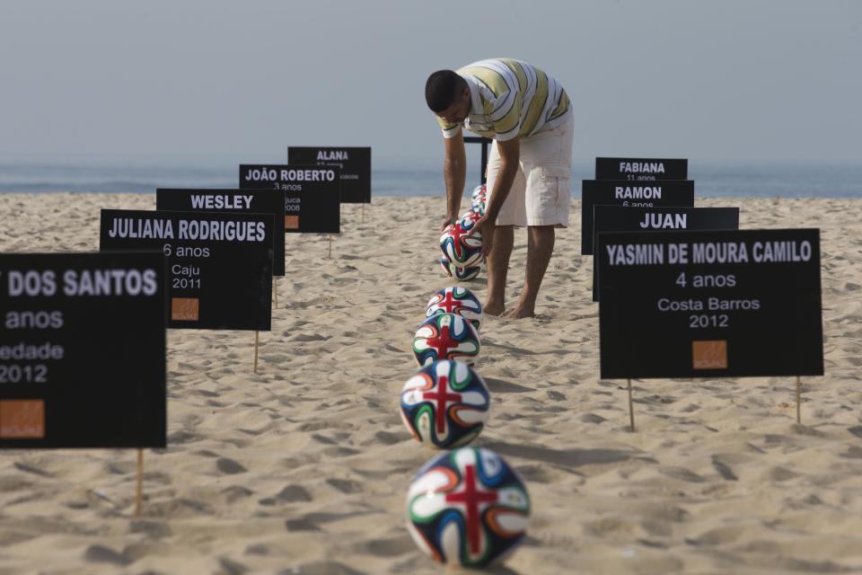 A protester places official 2014 World Cup soccer balls, called Brazuca, painted with red crosses next to the names and ages of children who have died from stray bullets during police operations, on Copacabana beach in Rio de Janeiro, Brazil, Wednesday, May 7, 2014. Organized by Rio de Paz, protesters say the money spent on World Cup preparations should have been used for the development of better schools, health care and improved security in shantytowns. (AP Photo/Hassan Ammar)