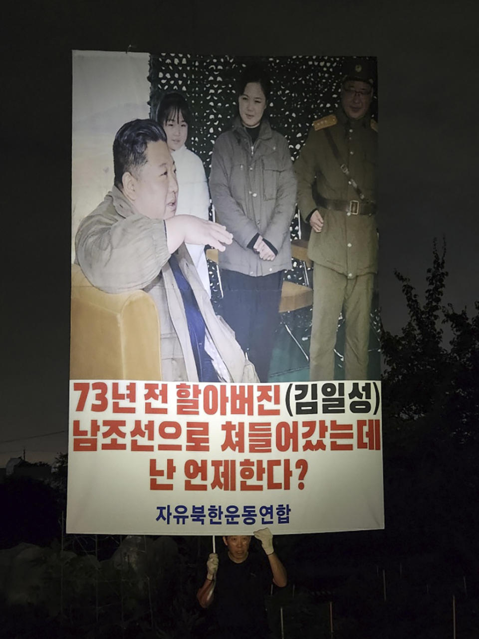 In this photo provided by Fighters For A Free North Kore, North Korean defector Park Sang-hak holds a banner showing an image of North Korean leader Kim Jong Un, left, his wife Ri Sol Ju, second from right, and his daughter, second from left, attached to one of the balloons to mark the 73rd anniversary of the outbreak of the Korean War, at Gimpo, South Korea, Sunday, June 25, 2023. The signs read "My grandfather (Kim Il Sung) invaded South Korea 73 years ago. When should I do the same?" (Fighters For A Free North Korea via AP).