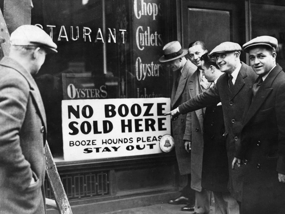 Men pointing at a sign in a store window that reads "no booze sold here. booze hounds please stay out."