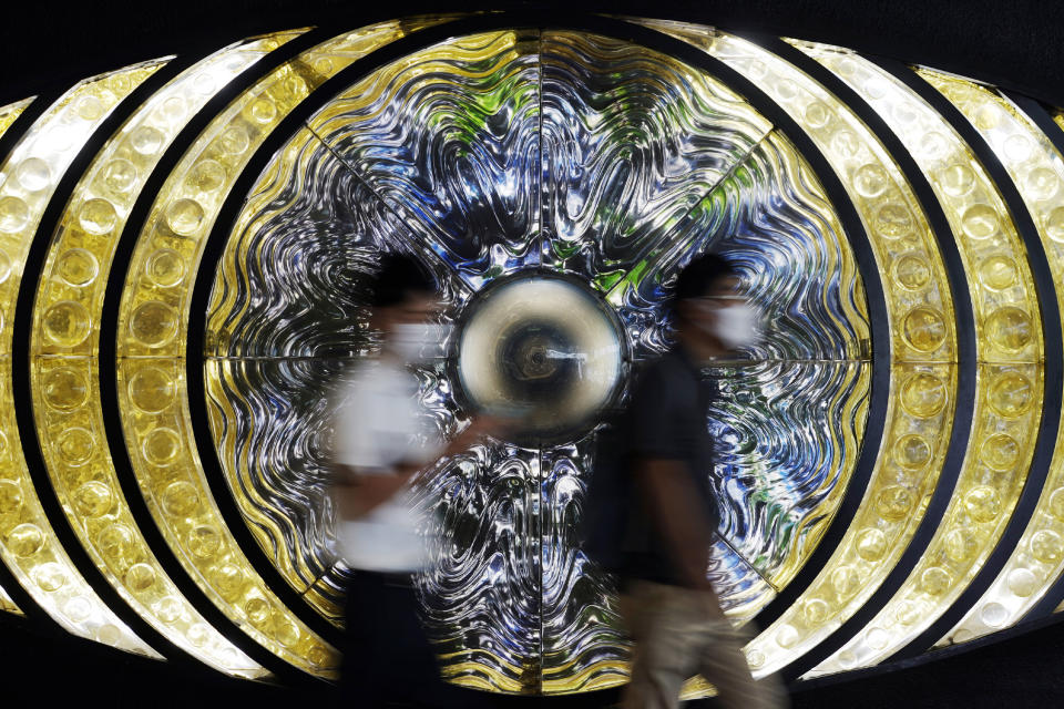 Men wearing face masks to help curb the spread of the coronavirus walk in front of art installation, Thursday, Aug. 27, 2020, in Tokyo. (AP Photo/Eugene Hoshiko)