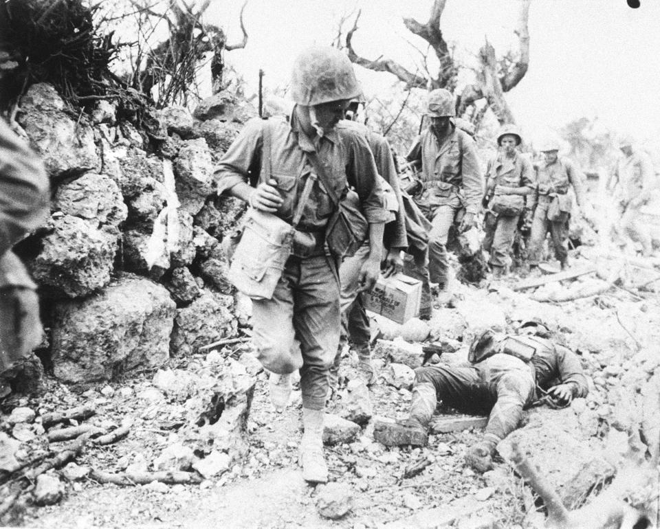 In this April, 1945, photo, a U.S. soldier walks past the body of a Japanese soldier in Okinawa, southern Japan. More than 200,000 people, about half of them civilians and about 12,500 American soldiers, died in the Battle of Okinawa, the deadliest in the Pacific War. (Kyodo News via AP)