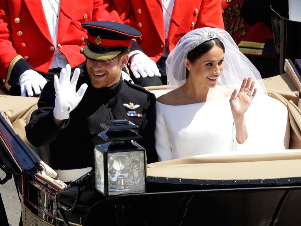 Meghan and Harry smiling and waving excitedly in their carriage in wedding attire.