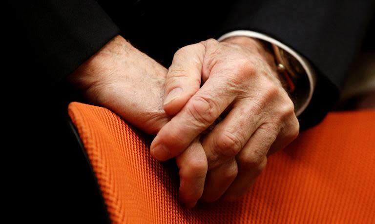 Formula One supremo Bernie Ecclestone puts his hands on a chair as he waits in the dock for the opening of his trial at court in Munich, southern Germany, on April 24, 2014