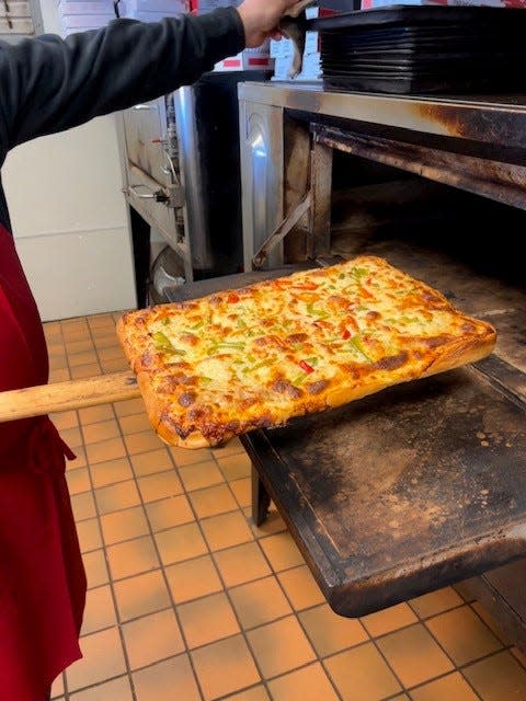 An O'Scugnizzo Pizzeria employee pulls a sausage and pepper pizza out of the oven.