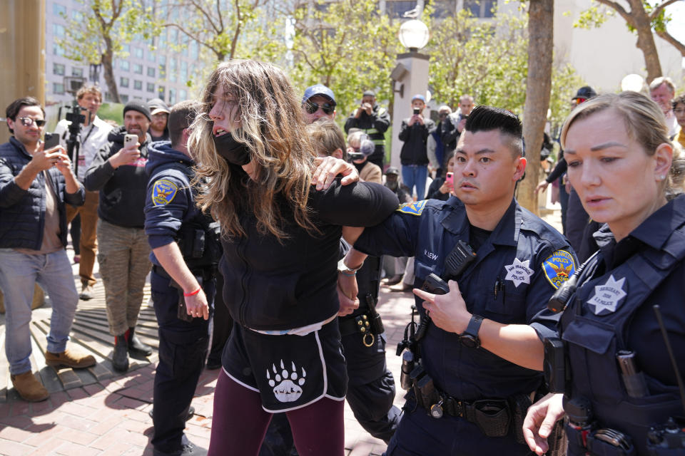 A protester who threw a brick at a color guard after a rare outdoor meeting of the Board of Supervisors is led away by police at UN Plaza in San Francisco, Tuesday, May 23, 2023. Mayor London Breed attempted to answer questions from supervisors demanding her administration do more to shut down open-air drug dealing, but the meeting had to be moved indoors to City Hall because of disruptions. (AP Photo/Eric Risberg)