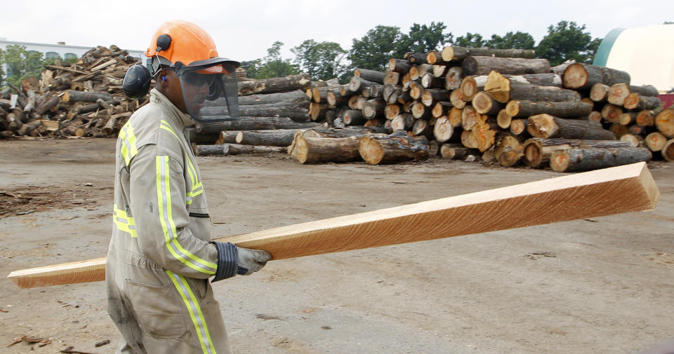 In this Wednesday, Aug. 15, 2012 photo, Andre Scott, of Jersey City, N.J., carries a piece of trimmed wood cut from discarded tree trunk at Citilog, in Newark, N.J. The Newark company takes unwanted trees from the so-called urban forest — parks, yards, streets and wherever else a tree might grow in a city — and turns them into furniture, flooring and other materials. (AP Photo/Mel Evans)