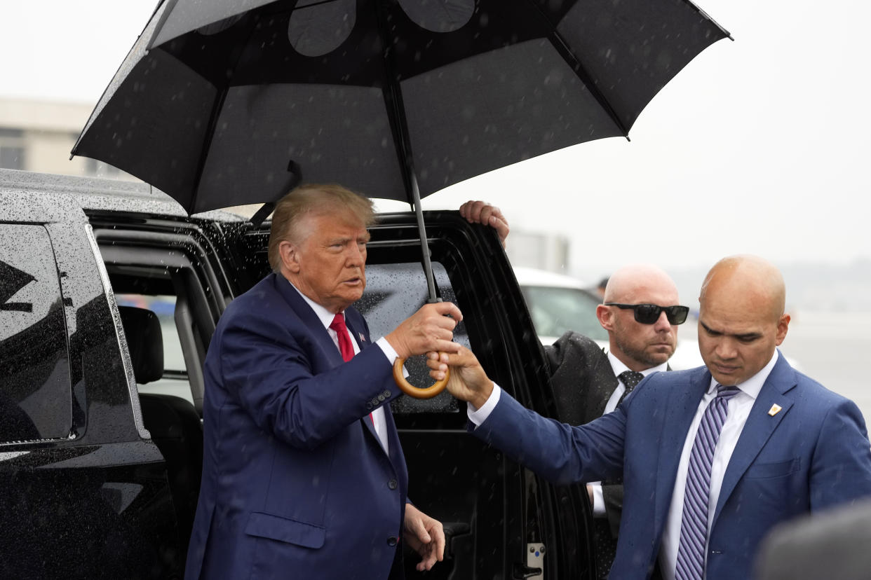 Valet Walt Nauta, looking down, hands Trump an umbrella as he descends from a limousine.