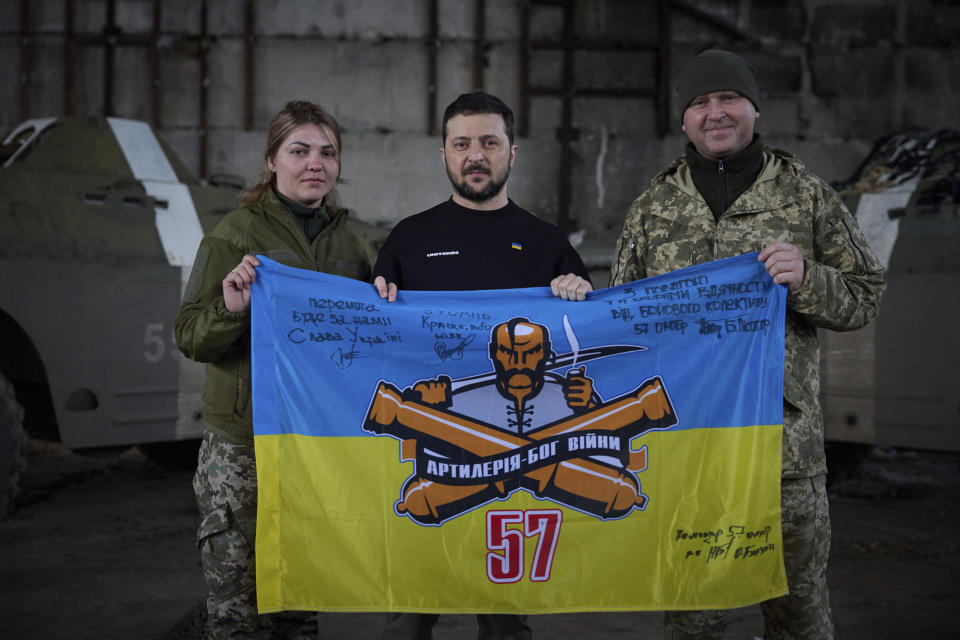 In this photo provided by the Ukrainian Presidential Press Office, Ukrainian president Volodymyr Zelenskyy, center, and Ukrainian soldiers hold the flag of a military unit at a position near Bakhmut, Donetsk region, Ukraine, Wednesday, March 22, 2023. (Ukrainian Presidential Press Office via AP)