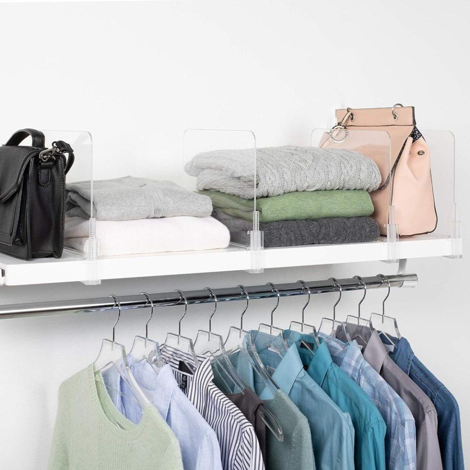 Clear shelf dividers organize clothing items on a closet shelf above hanging clothes