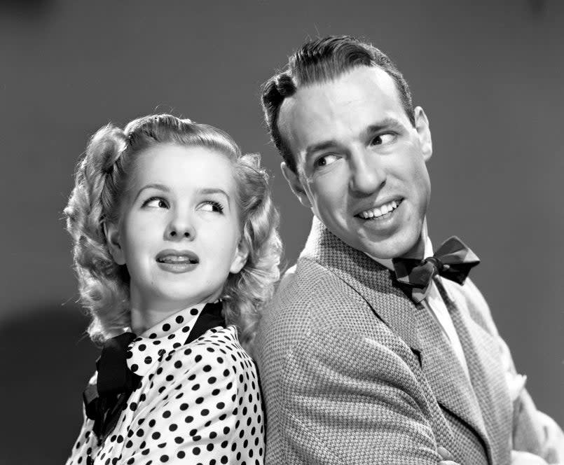 Two vintage Hollywood stars, the man in a tweed suit and bow tie, the woman in a polka dot dress with a bow collar