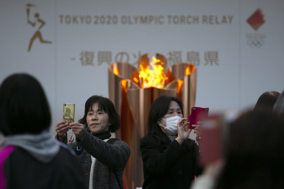 FILE - In this March 24, 2020, file photo, people take pictures with the Olympic Flame during a ceremony in Fukushima City, Japan. The Olympic flame has been removed from public display in Japan, and it's not clear when it will reappear again or where. The flame arrived in Japan from Greece on March 26. (AP Photo/Jae C. Hong, File)