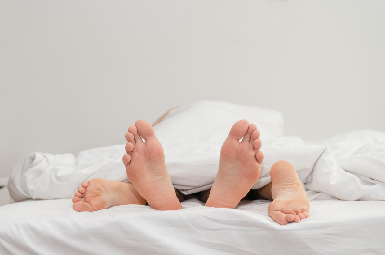 Feet of couple in love on the bed having sex under white blankets