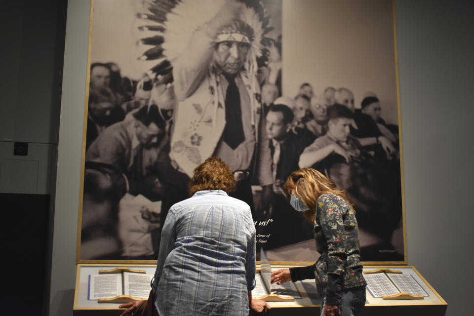 In this Wednesday, May 19, 2021, photo, people tour an exhibit showing a photo of late Chief Thomas Spotted Wolf at a hearing objecting to the construction of Garrison Dam, at the MHA Nation Interpretive Center on the Fort Berthold Indian Reservation in New Town, North Dakota. The $30 million cultural center in New Town pieces together the tribes' fractured past through displays and artifacts. A sound studio captures stories from elders who lived through dam construction and flooding of 135,000 acres (55,000 hectares) along the Missouri. (AP Photo/Matthew Brown)