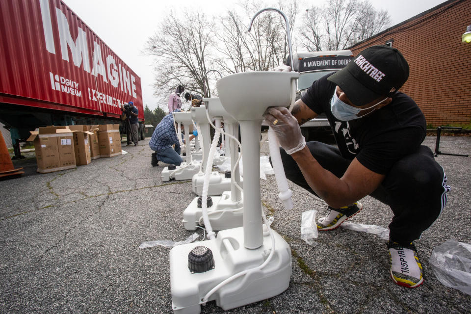 Grammy award-winning hip hop recording artist Lecrae assembles a portable wash station on Thursday, March 19, 2020 in College Park, Georgia. The wash stations were distributed by Lecrae and volunteers with Love Beyond Walls, a non-profit, throughout Atlanta in areas with a high density of homeless persons. (AP Photo/ Ron Harris)