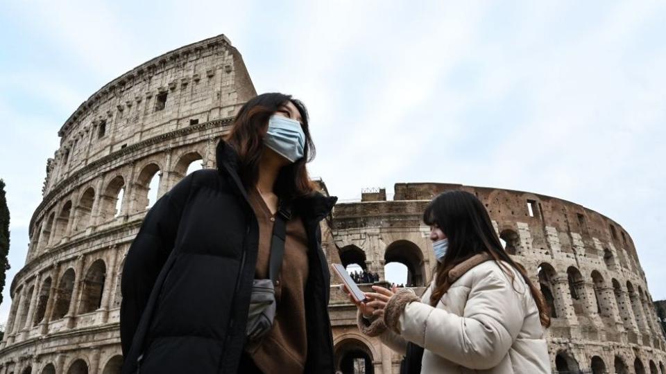 Personas con mascarillas frente al coliseo romano.