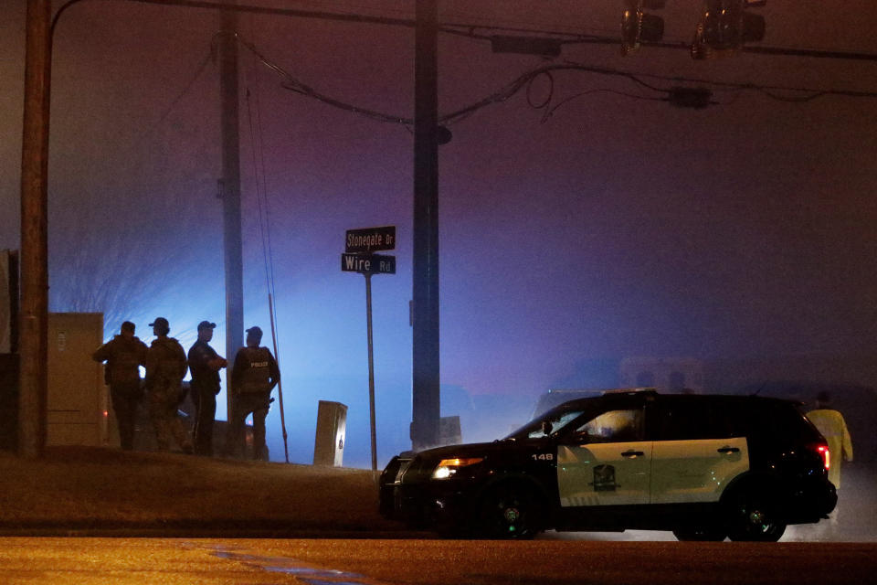 Law enforcement officers stand at the corner Stonegate Drive and Wire Road in Auburn, Ala., on Friday, Feb. 15, 2019, which is the entrance of an apartment complex where officers confronted two suspects who were wanted in connection to the shooting of an Auburn police officer and the attempted robbery of an Auburn business. (Emily Enfinger/Opelika-Auburn News via AP)