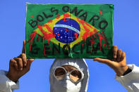 FILE - In this May 26, 2021 file photo, a demonstrator holds an image of the Brazilian flag covered in fake blood and the Portuguese phrase "Bolsonaro Genocide" during an anti-government protest by unions against President Jair Bolsonaro's policies to fight the COVID-19 pandemic in Brasilia, Brazil. Brazil's Senate is publicly investigating how the death toll got so high, focusing on why Bolsonaro's government ignored opportunities to buy vaccines for months. (AP Photo/Eraldo Peres, File)