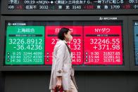Woman walks past an electronic board showing world benchmarks outside a brokerage, in Tokyo