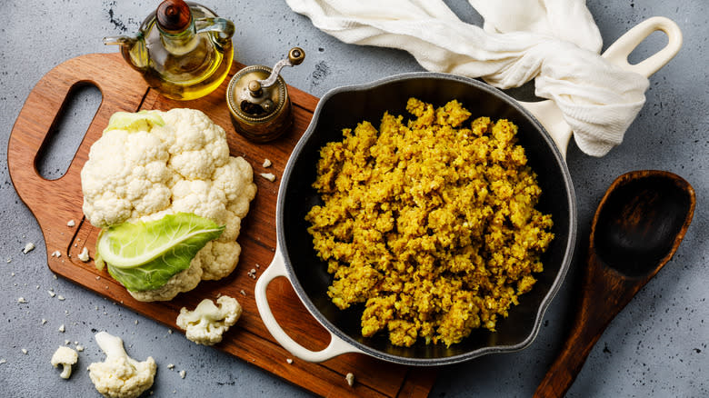 Cauliflower rice in skillet with fresh cauliflower