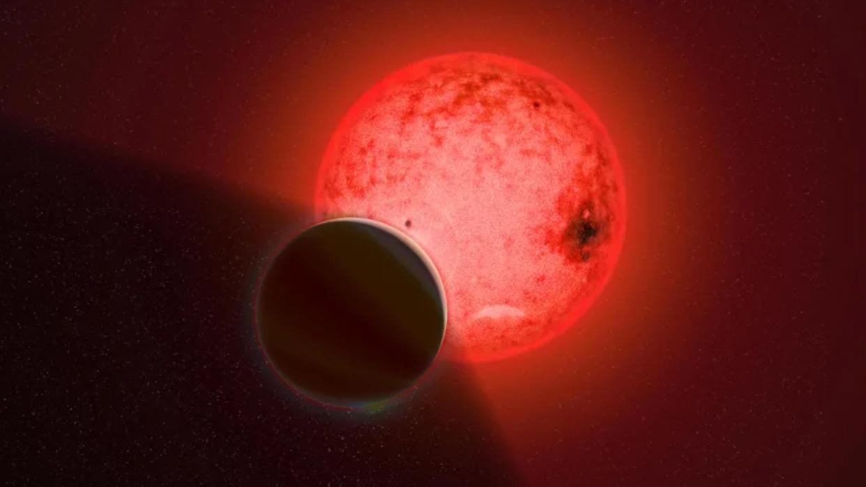  A dark planet passes in front of a bright red star. 