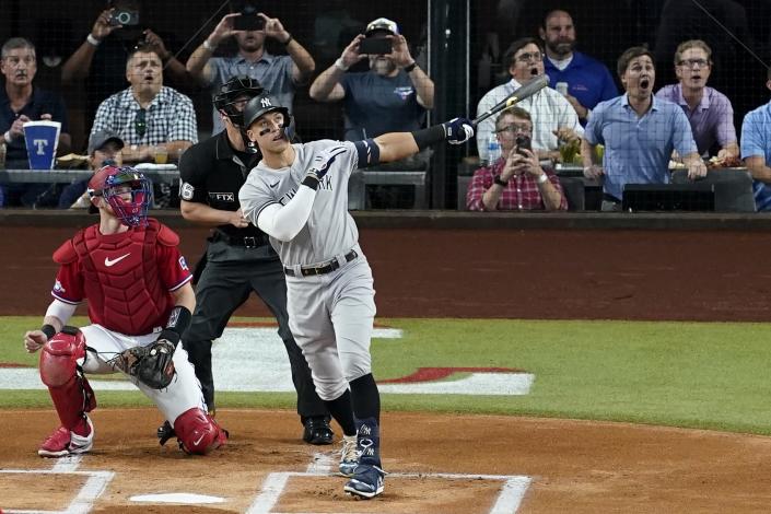 New York Yankees' Aaron Judge follows through on a solo home run, his 62nd of the season, as Texas Rangers catcher Sam Huff, left, and umpire Randy Rosenberg, rear, look on in the first inning of the second baseball game of a doubleheader in Arlington, Texas, Tuesday, Oct. 4, 2022. With the home run, Judge set the AL record for home runs in a season, passing Roger Maris. (AP Photo/Tony Gutierrez)