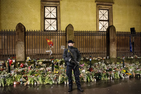 A guard stands in front of bouquets of flowers left as memorials outside a Jewish synagogue during a memorial service for security guard Dan Uzan and filmmaker Finn Noergaard, who were killed during shooting attacks last week, in Copenhagen, Denmark February 24, 2015. REUTERS/Bax Lindhardt/Scanpix