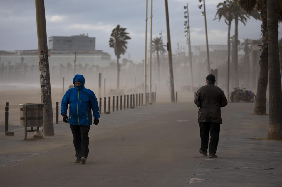 People walk along the beach during strong winds in Barcelona, Spain, Monday, Jan. 20, 2020. Two people have died as storms carrying heavy snowfalls and gale-force winds lashed many parts of Spain on Monday. The storm has forced the closure of Alicante airport and some 30 roads in eastern region. Six provinces are on top alert. (AP Photo/Emilio Morenatti)