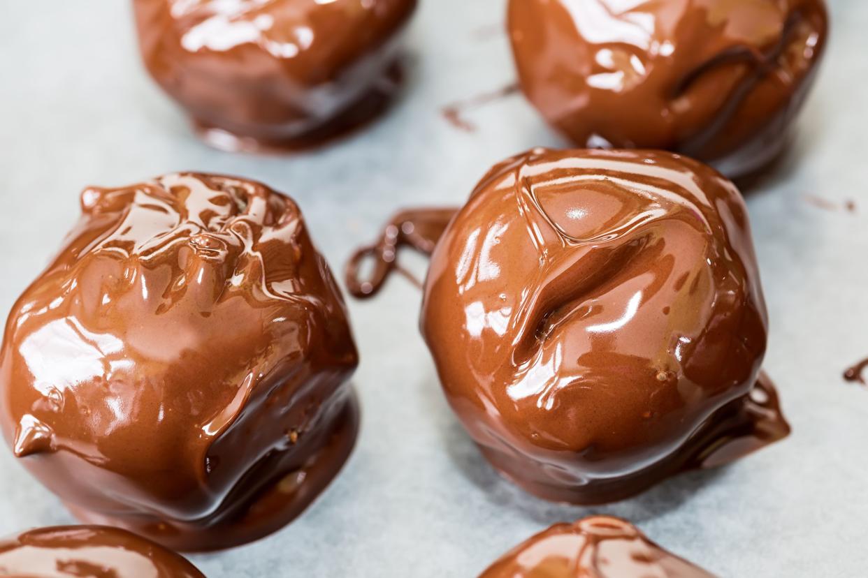 Closeup of six easy no-bake peanut butter balls on wax paper, two are in the center with two on top and two on bottom of image