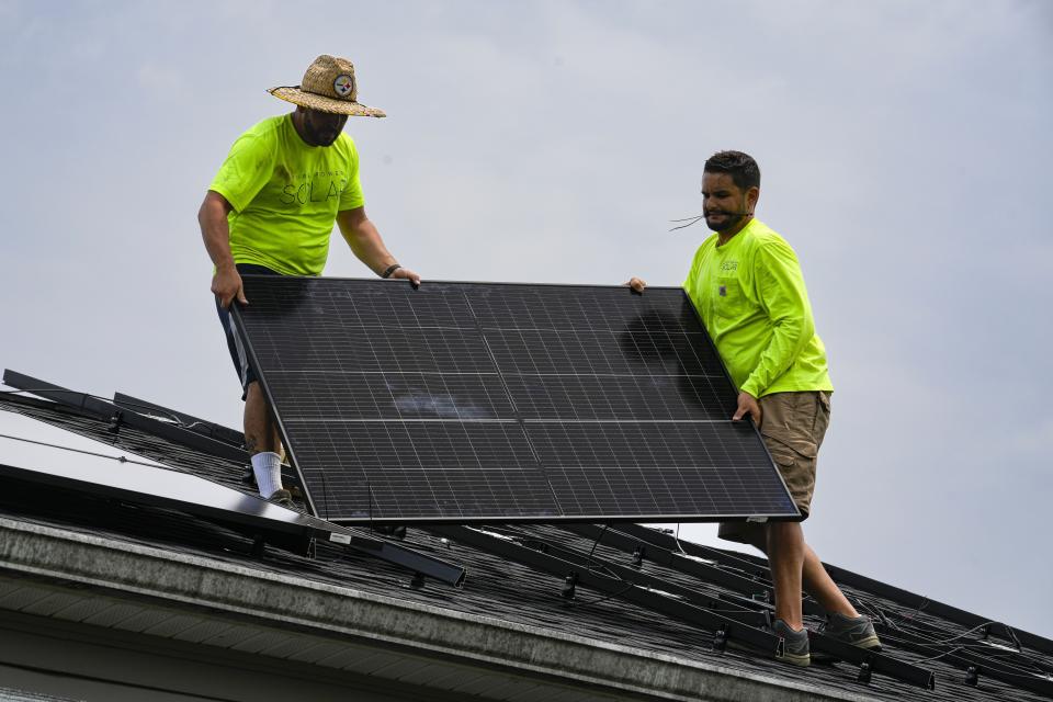 Even Berrios, left, and Nicholas Hartnett, owner of Pure Power Solar, install a solar panel on the roof of a home in Frankfort, Ky., Monday, July 17, 2023. Since passage of the Inflation Reduction Act, it has boosted the U.S. transition to renewable energy, accelerated green domestic manufacturing, and made it more affordable for consumers to make climate-friendly purchases, such as installing solar panels on their roofs. (AP Photo/Michael Conroy)