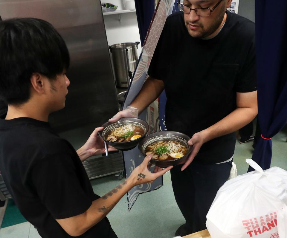 Devin Sarnowski, right, steps out of the kitchen and hands two bowls of shoyu ramen to server Chris Dator at Oishi Japanese Kitchen in Bremerton on Monday, Nov. 20, 2023.