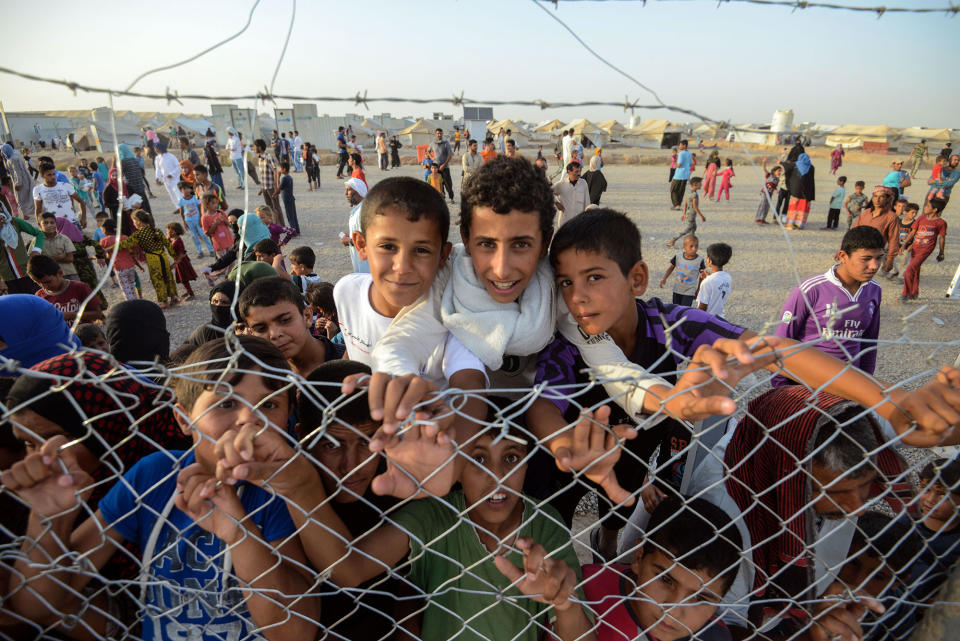 <p>Displaced Iraqi children stand behind a fence at the Hasan Sham camp for Internally Displaced People on June 10, 2017. (Photo: Mohaned El-Shahed/AFP/Getty Images) </p>