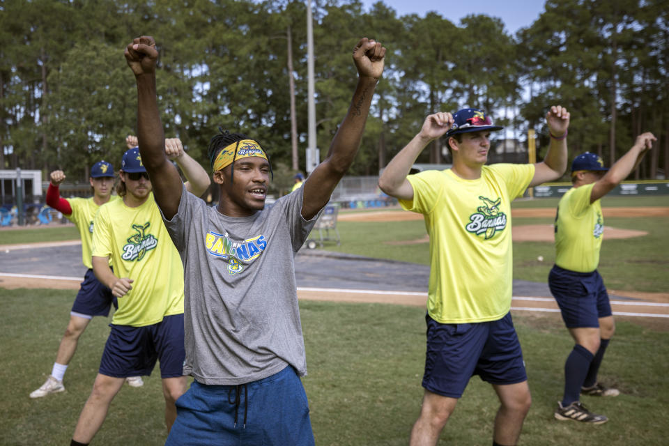 FILE - Savannah Bananas first base coach Maceo Harrison, foreground, teaches a dance routine to members of the team before they play the Florence Flamingos, Tuesday, June 7, 2022, in Savannah, Ga. The Savannah Bananas, who became a national sensation with their irreverent style of baseball, are leaving the Coastal Plains League to focus full attention on their professional barnstorming team. Owner Jesse Cole made the announcement in a YouTube video, saying “we'll be able to bring the Savannah Bananas to more people in Savannah and around the world."(AP Photo/Stephen B. Morton, File)