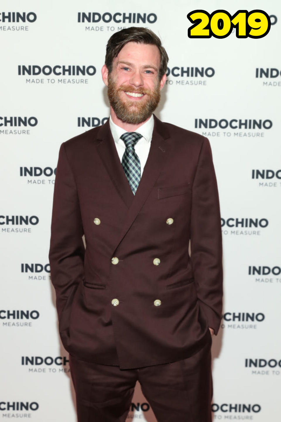 Un hombre con traje cruzado, de pie frente a un telón de fondo de Indochino, lee "Indochino hecho a medida"